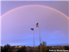 Rainbow appearing over flags on flagpoles. 