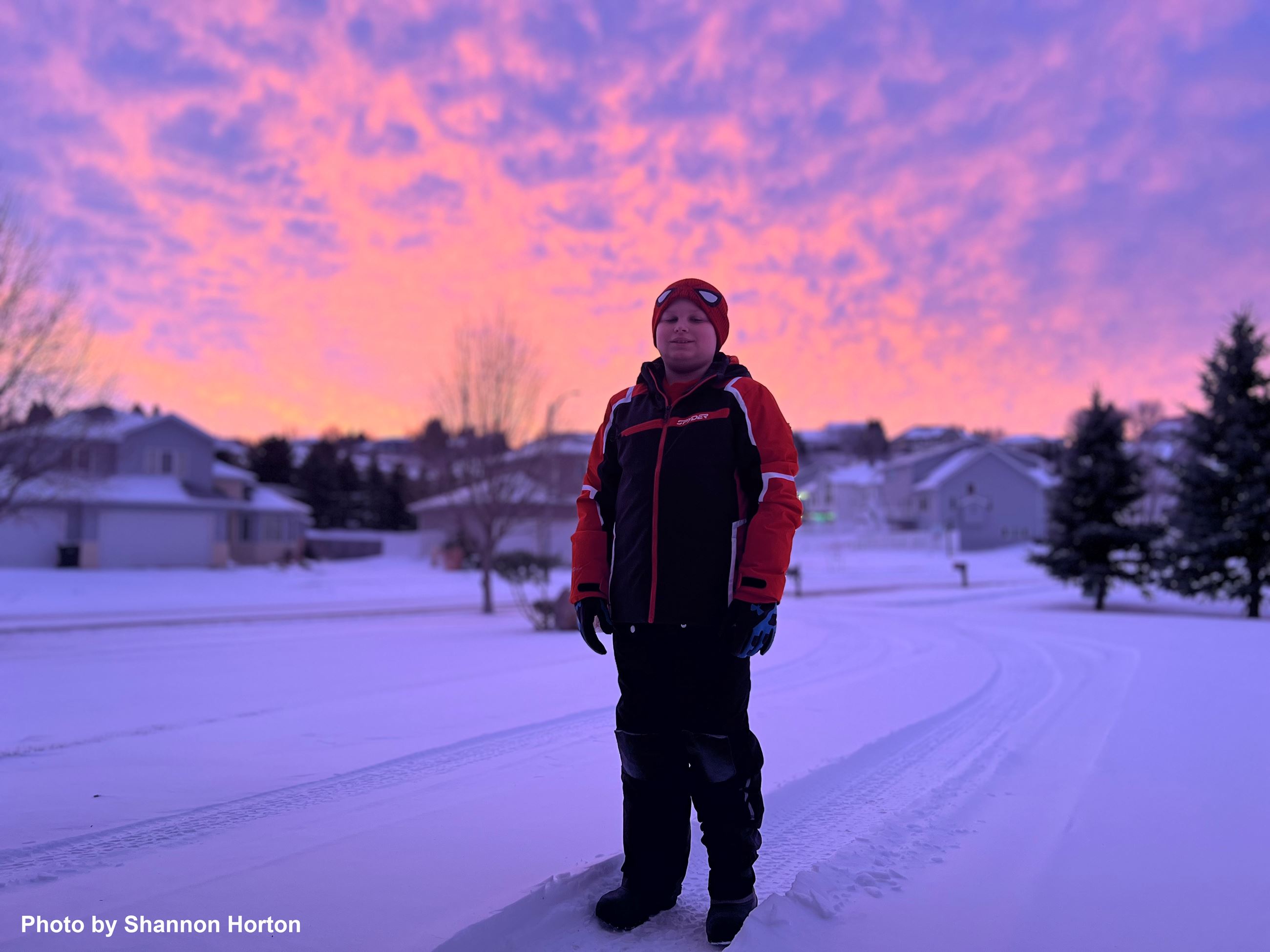 A boy standing in front of a winter sunset. 